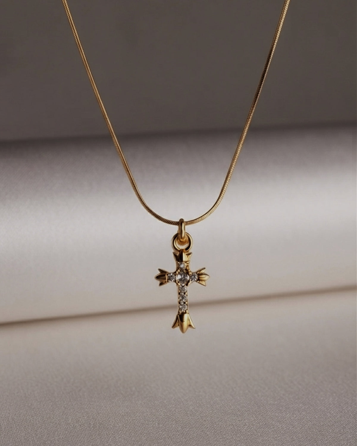 An ornate gothic cross with fleur-de-lis edges and a line of pave stones. Anti-tarnish, waterproof gold-tone stainless steel. Shop Zorelle India.